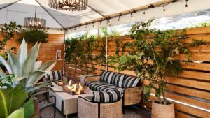Interior dining area with wooden slat walls, striped patio furniture, a fire pit and greenery